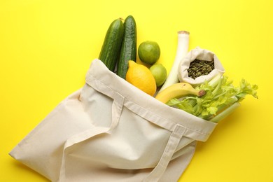 Photo of Eco bag with vegetables, fruits and pumpkin seeds on yellow background, top view