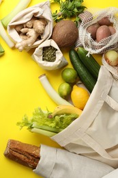 Photo of Eco bags with different food products on yellow background, flat lay