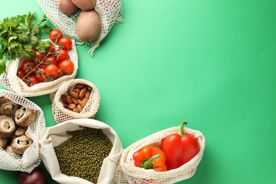 Photo of Eco bags with different food products on green background, flat lay. Space for text