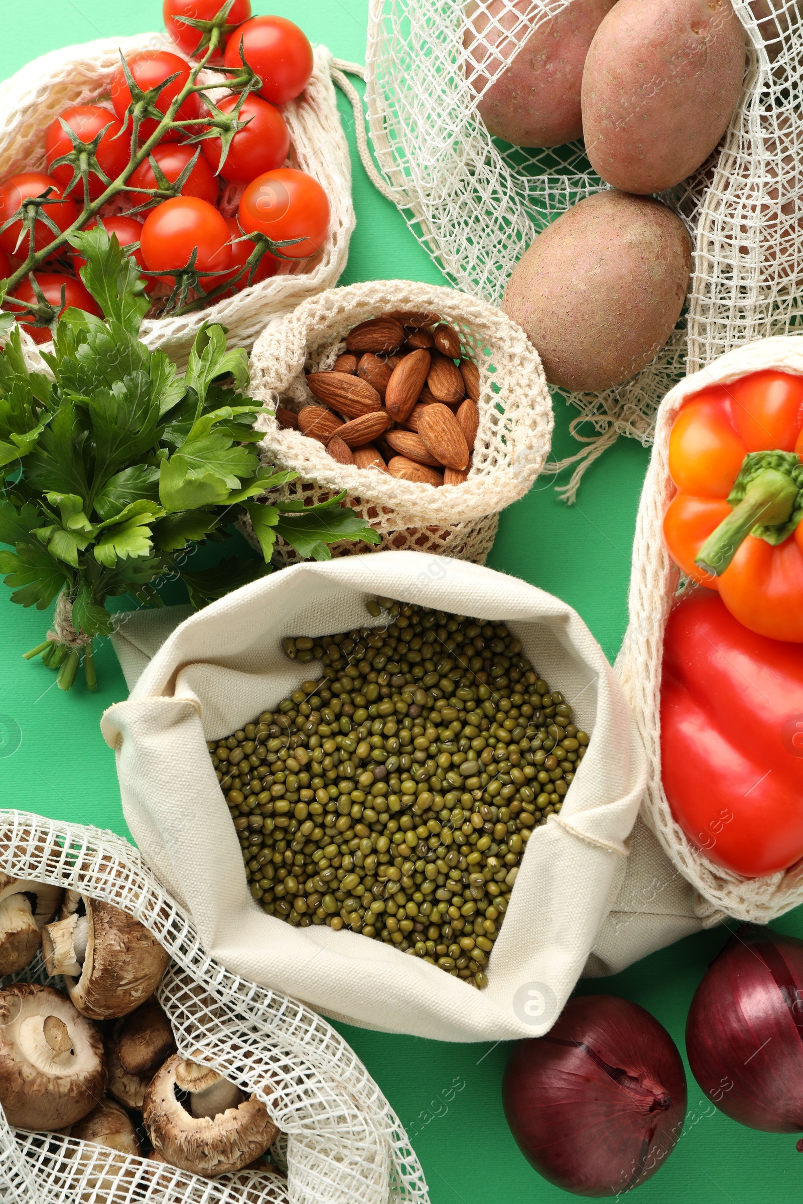 Photo of Eco bags with different food products on green background, flat lay