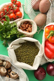 Photo of Eco bags with different food products on green background, flat lay