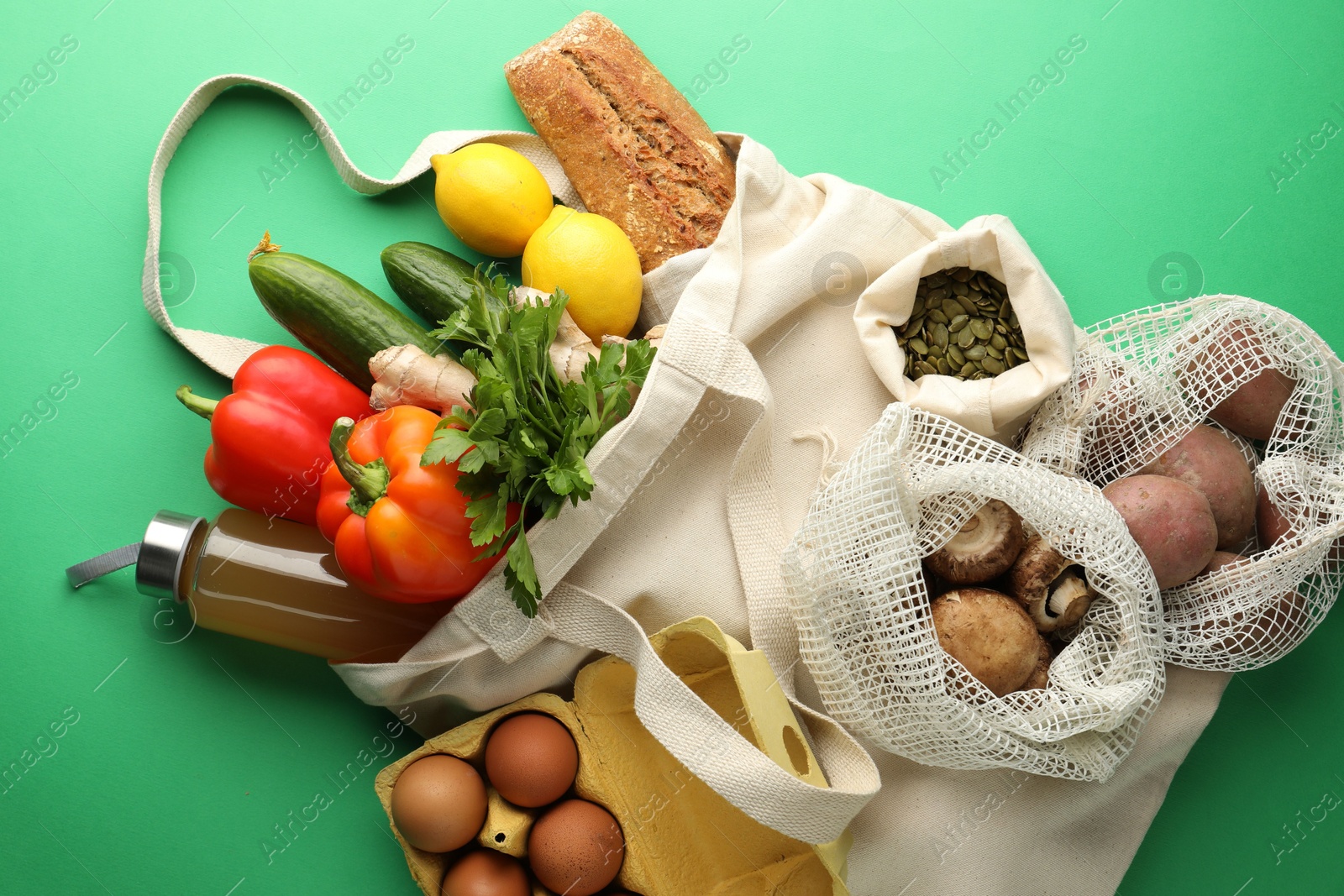 Photo of Eco bags with different food products on green background, flat lay