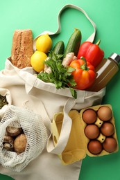 Photo of Eco bags with different food products on green background, flat lay