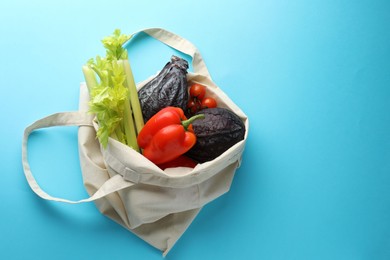 Photo of Eco bag with different vegetables on light blue background, top view. Space for text