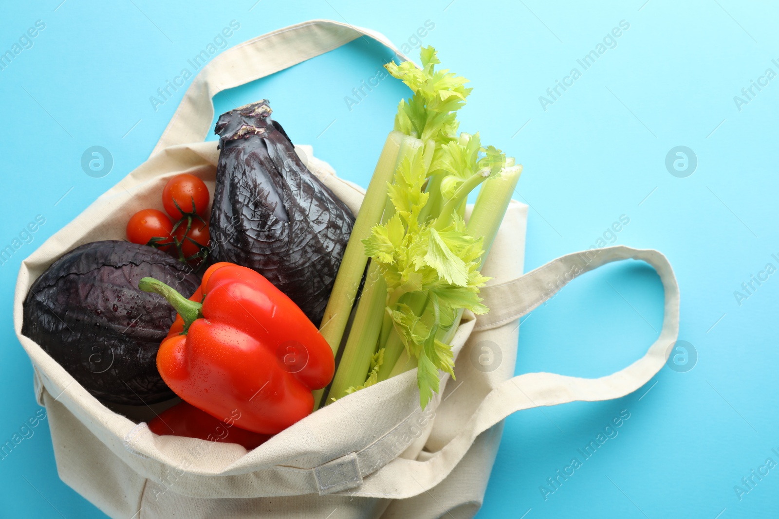 Photo of Eco bag with different vegetables on light blue background, top view