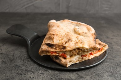 Photo of Halves of tasty calzone with meat, cheese and tomato on grey textured table, closeup