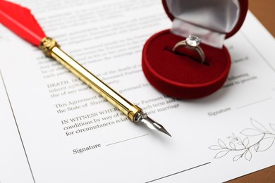 Photo of Marriage contract, pen and ring on brown background, closeup