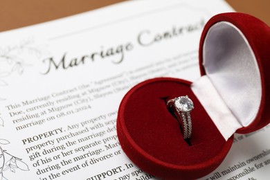 Photo of Marriage contract and ring on brown background, closeup