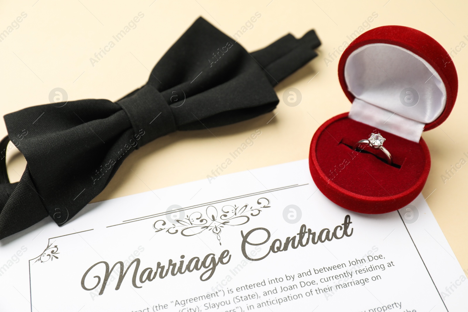 Photo of Marriage contract, bowtie and ring on beige table, closeup