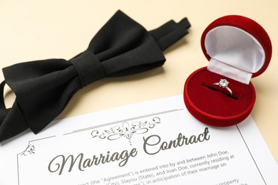 Photo of Marriage contract, bowtie and ring on beige table, closeup