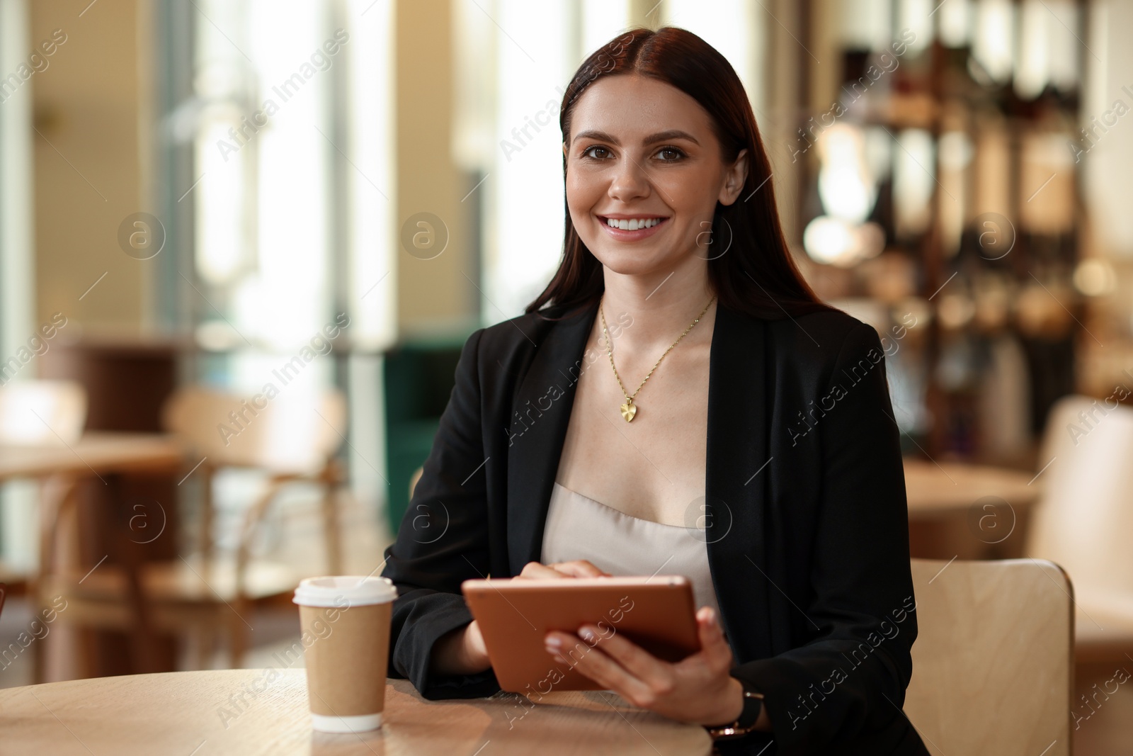 Photo of Woman in stylish formal suit with tablet and coffee at table indoors