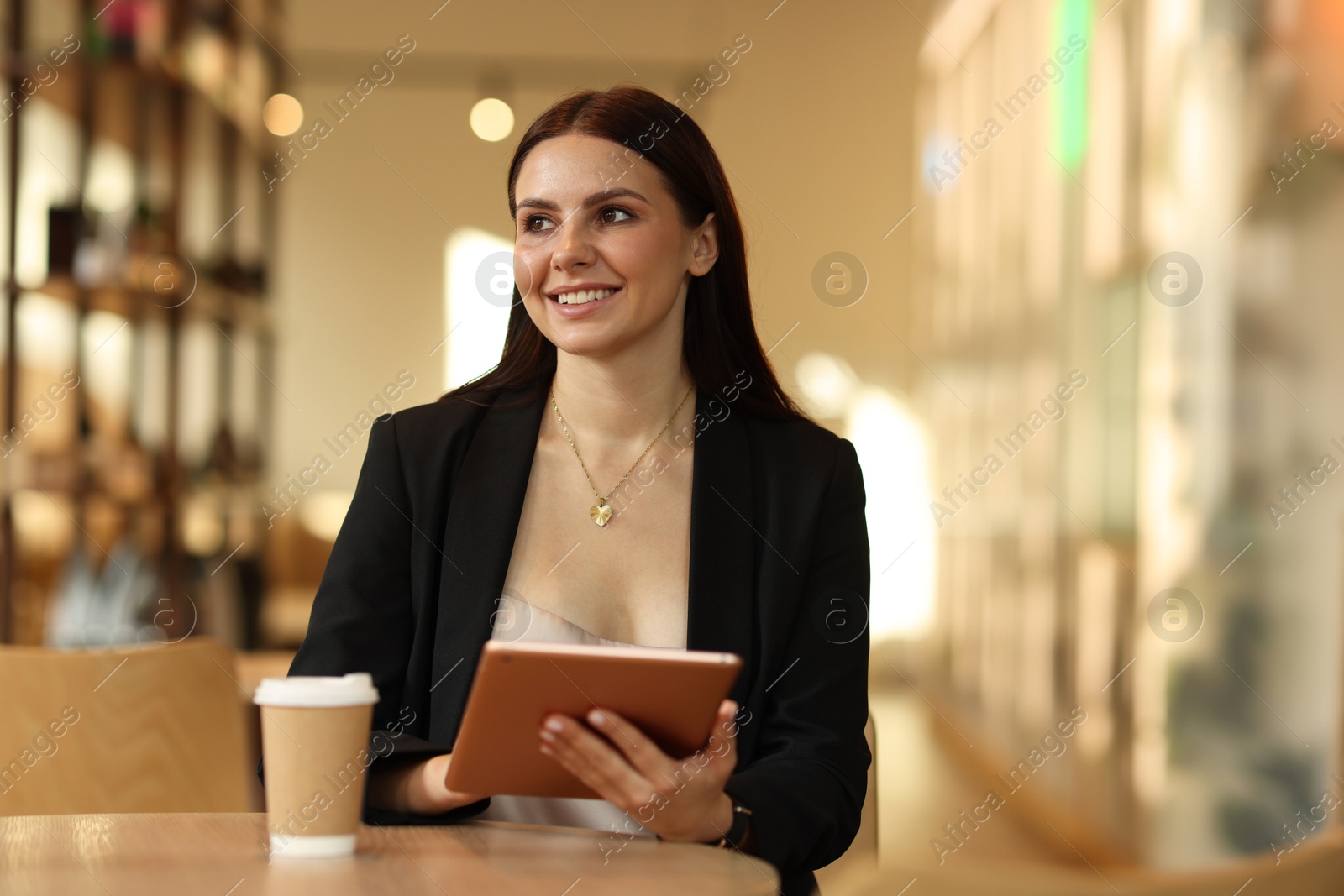 Photo of Woman in stylish formal suit with tablet and coffee at table indoors