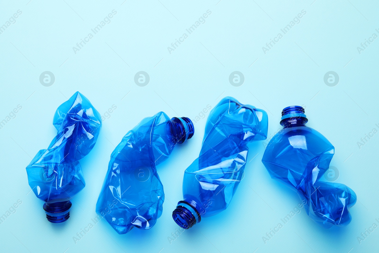 Photo of Crumpled plastic bottles on light blue background, flat lay