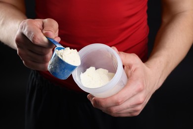 Sportsman adding protein into shaker on dark background, closeup