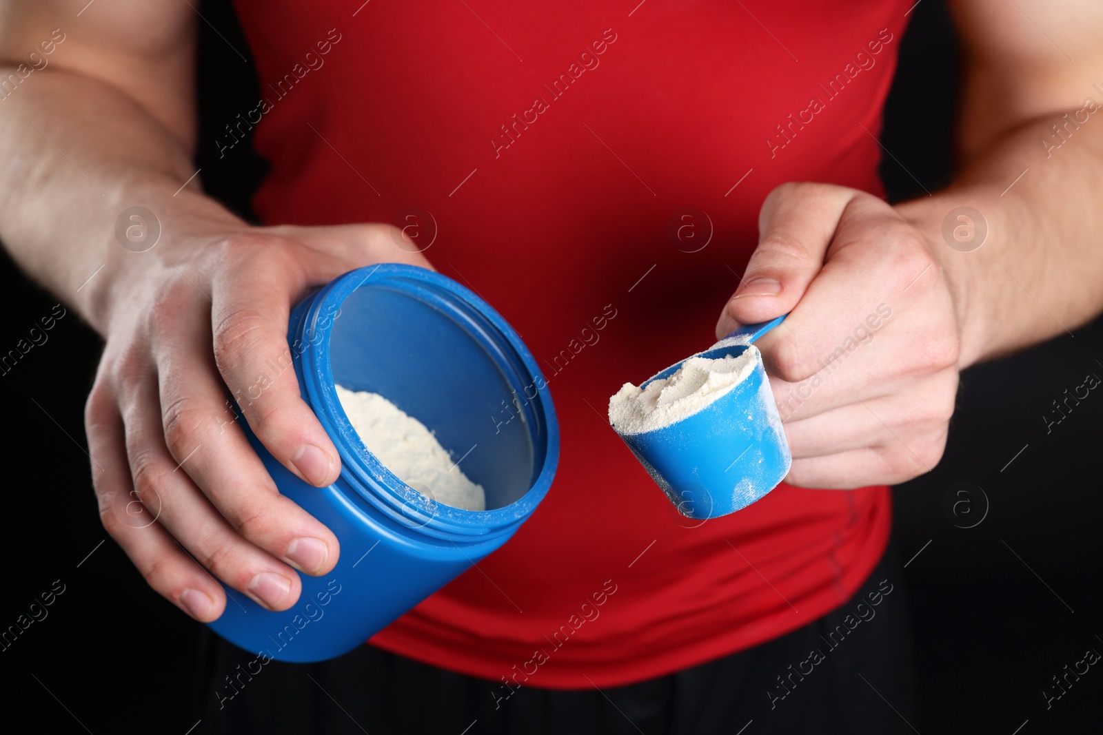 Photo of Sportsman taking protein with scoop on dark background, closeup