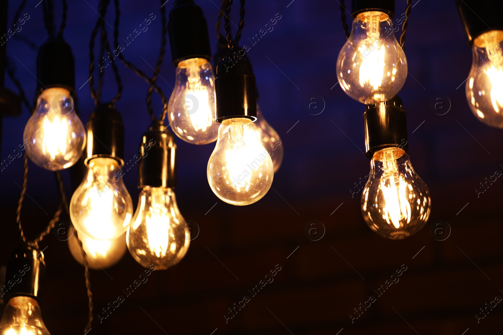 Photo of Glowing light bulbs hanging on dark background, closeup