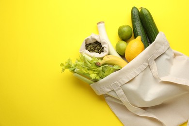 Photo of Eco bag with vegetables, fruits and pumpkin seeds on yellow background, top view. Space for text