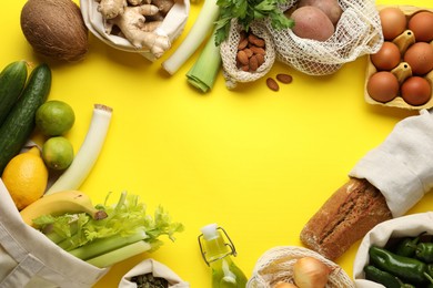 Photo of Frame of eco bags with different food products on yellow background, flat lay. Space for text