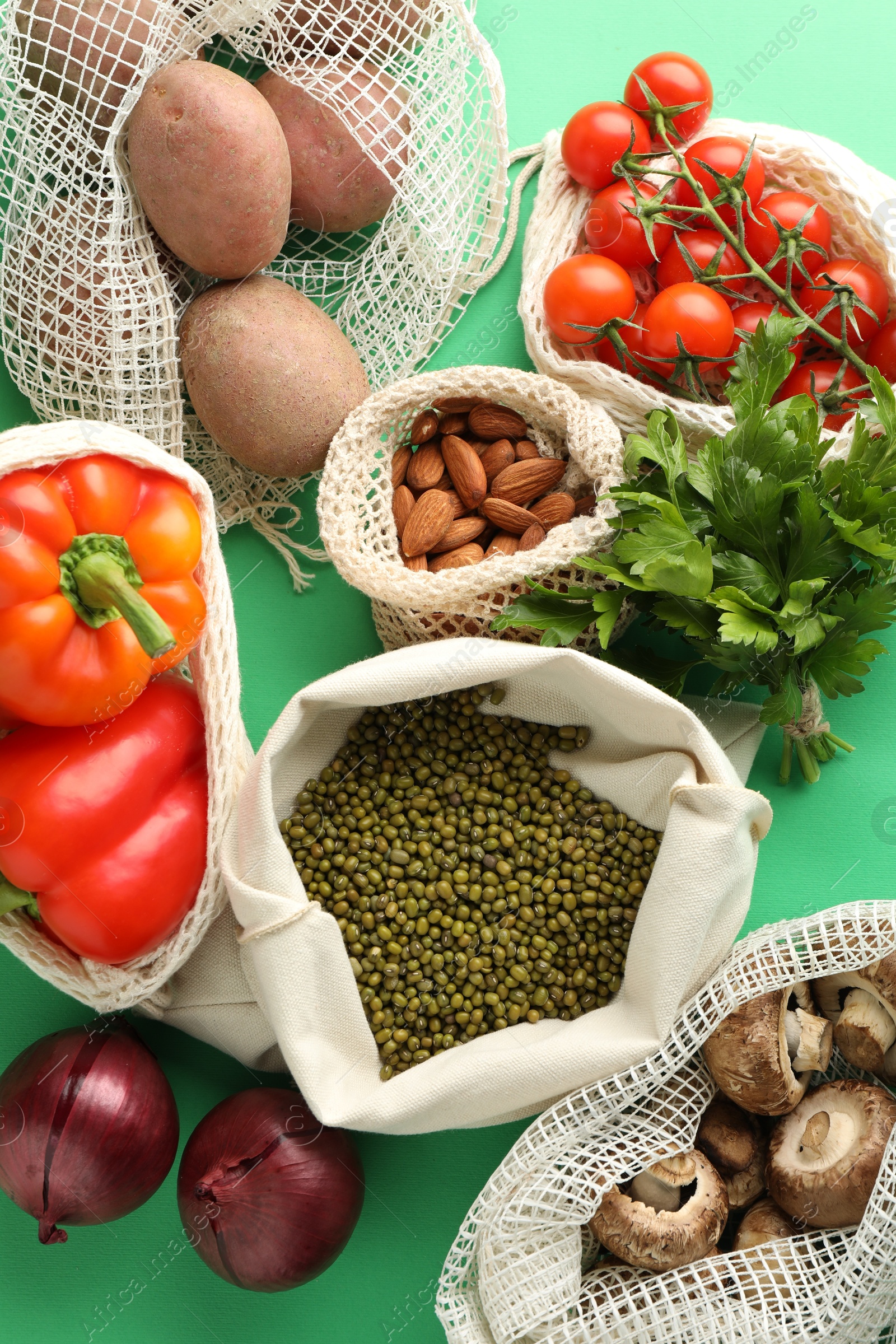 Photo of Eco bags with different food products on green background, flat lay