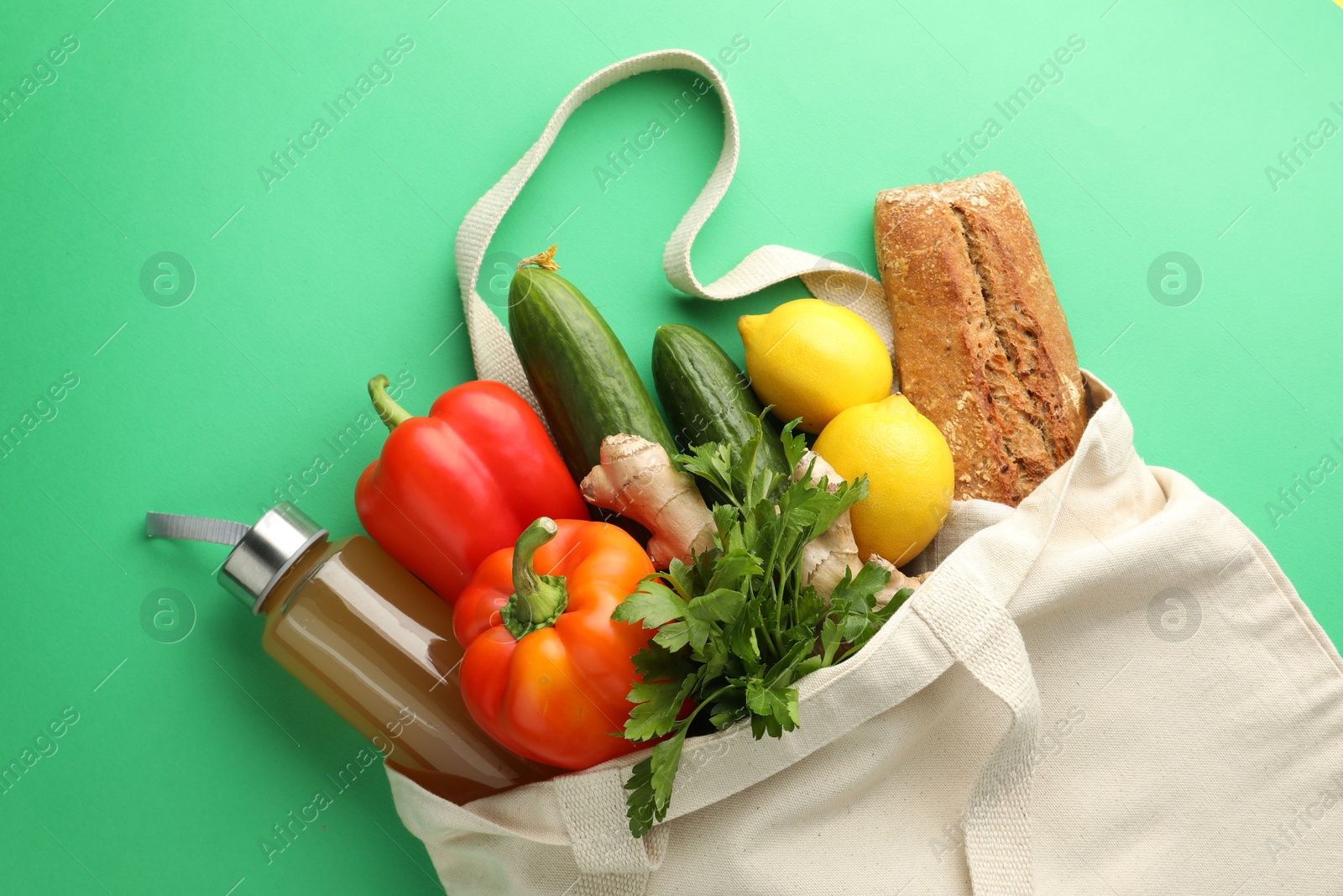 Photo of Eco bag with different food products and juice on green background, top view