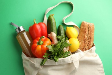 Photo of Eco bag with different food products and juice on green background, top view