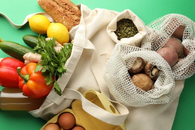 Photo of Eco bags with different food products on green background, flat lay