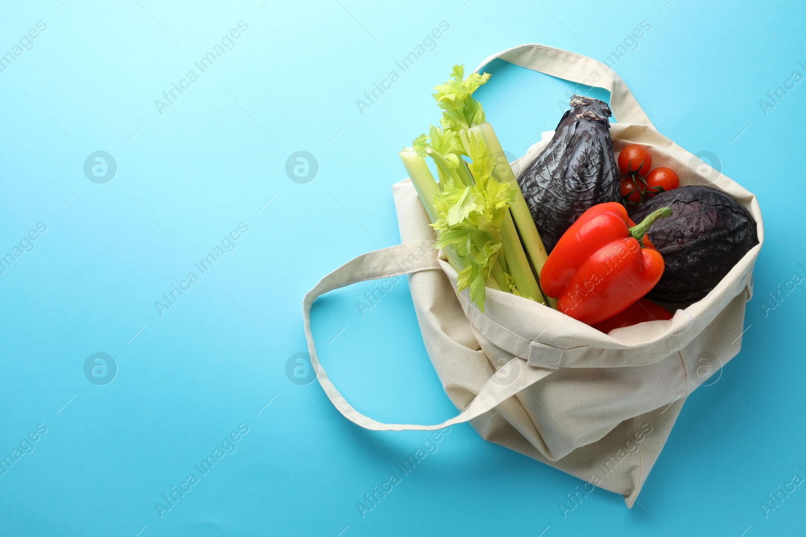 Photo of Eco bag with different vegetables on light blue background, top view. Space for text