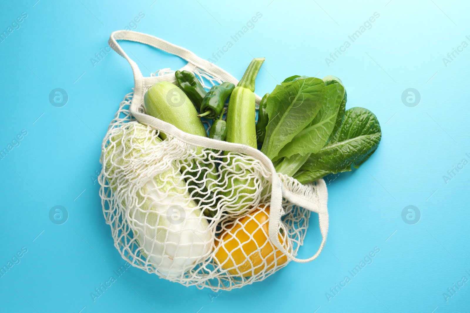 Photo of Net bag with products on light blue background, top view. Eco friendly lifestyle