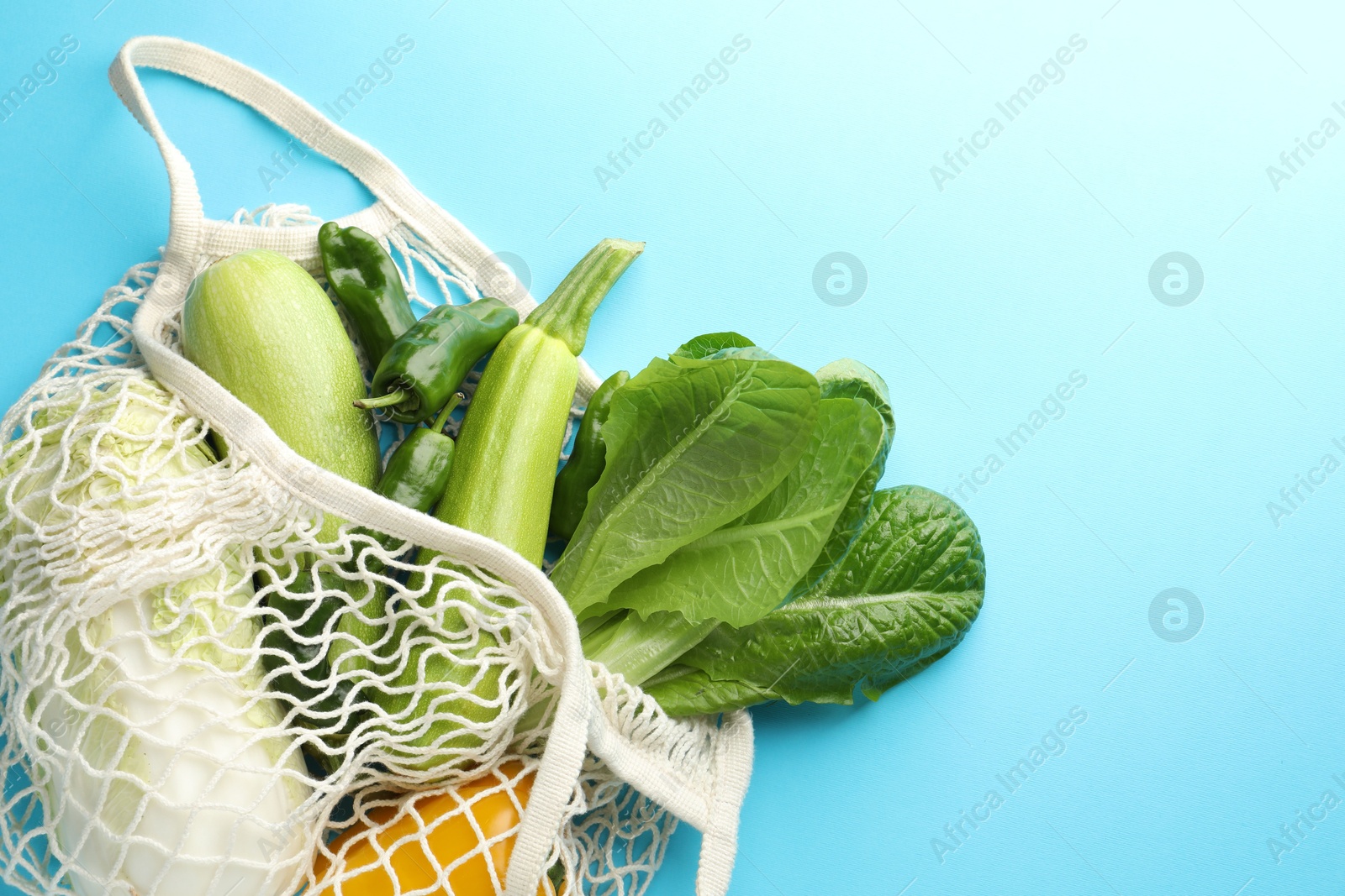 Photo of Net bag with products on light blue background, top view and space for text. Eco friendly lifestyle