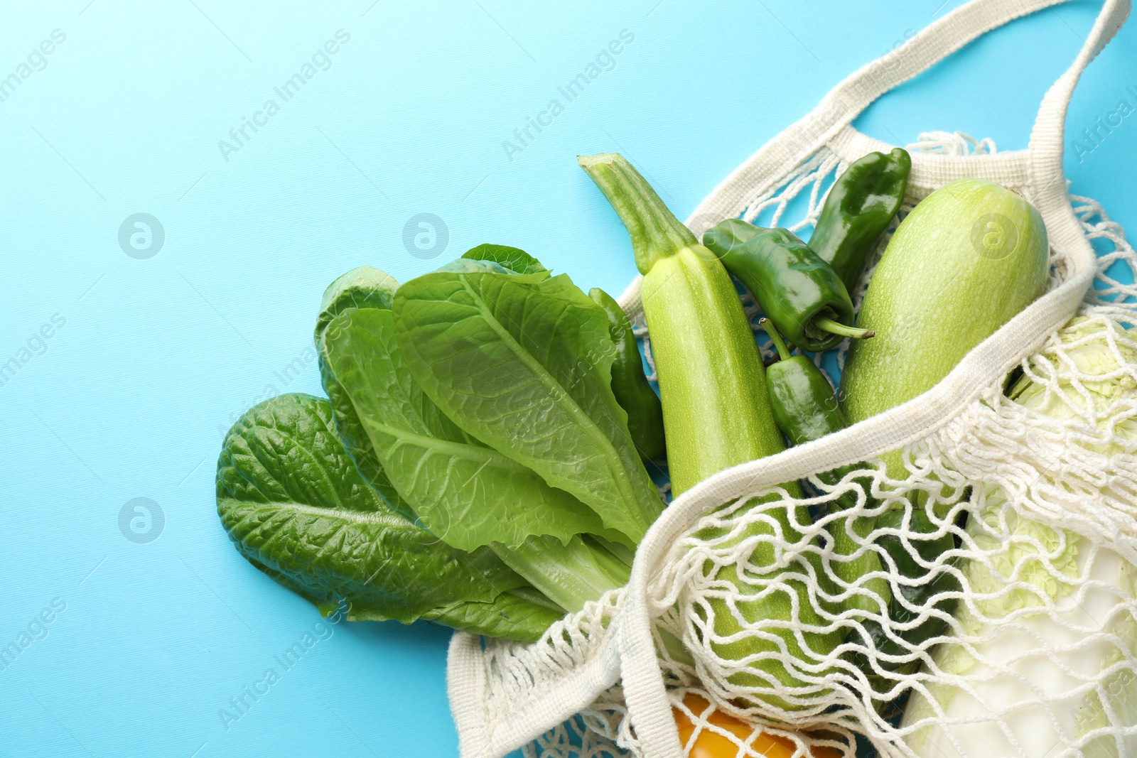 Photo of Net bag with products on light blue background, top view and space for text. Eco friendly lifestyle