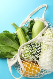 Photo of Net bag with products on light blue background, top view. Eco friendly lifestyle