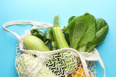 Photo of Net bag with products on light blue background, top view. Eco friendly lifestyle