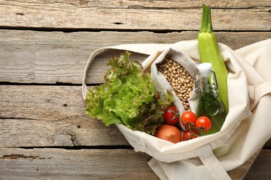 Photo of Shopper bag with products on wooden background, top view and space for text. Eco friendly lifestyle