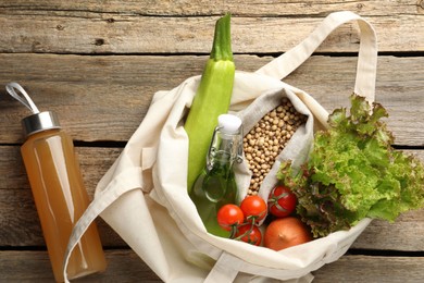 Photo of Shopper bag with products on wooden background, top view. Eco friendly lifestyle