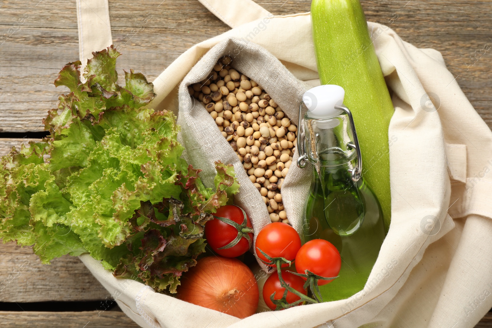 Photo of Shopper bag with products on wooden background, closeup. Eco friendly lifestyle