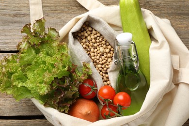 Photo of Shopper bag with products on wooden background, closeup. Eco friendly lifestyle