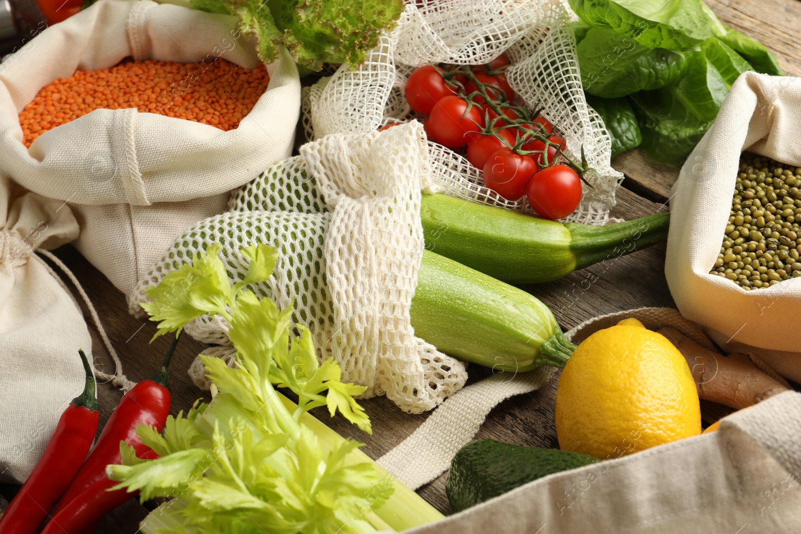 Photo of Shopper bags with products on wooden background, closeup. Eco friendly lifestyle