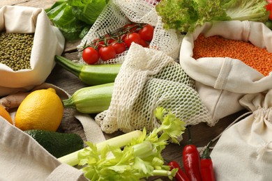 Photo of Shopper bags with products on wooden background, closeup. Eco friendly lifestyle