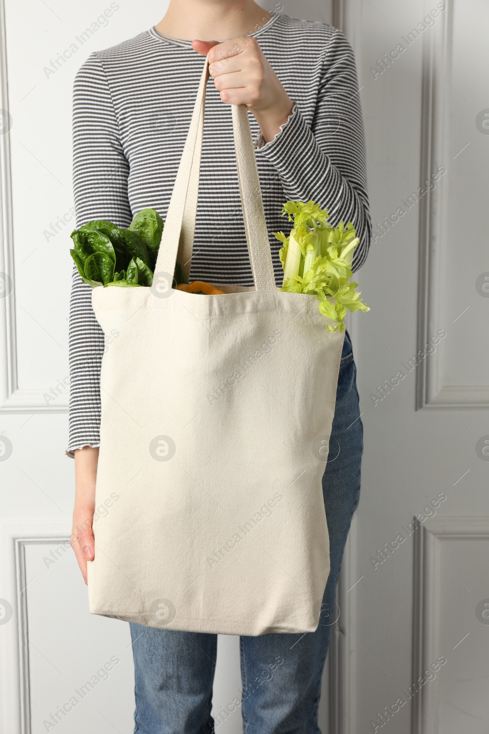 Photo of Woman holding shopper bag with groceries near white wall, closeup. Eco friendly lifestyle