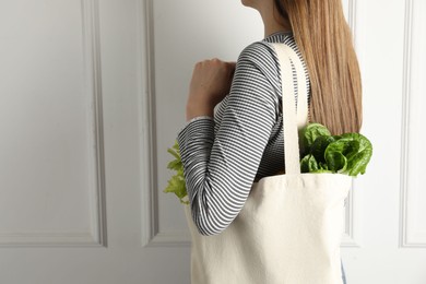 Photo of Woman holding shopper bag with groceries near white wall, closeup and space for text. Eco friendly lifestyle