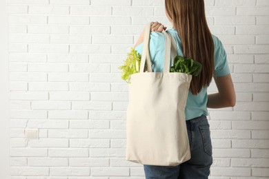 Photo of Woman holding shopper bag with groceries near white brick wall, closeup and space for text. Eco friendly lifestyle