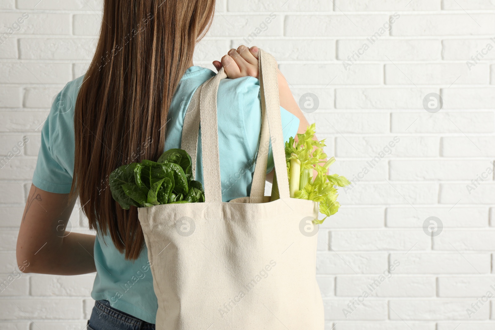 Photo of Woman holding shopper bag with groceries near white brick wall, closeup and space for text. Eco friendly lifestyle