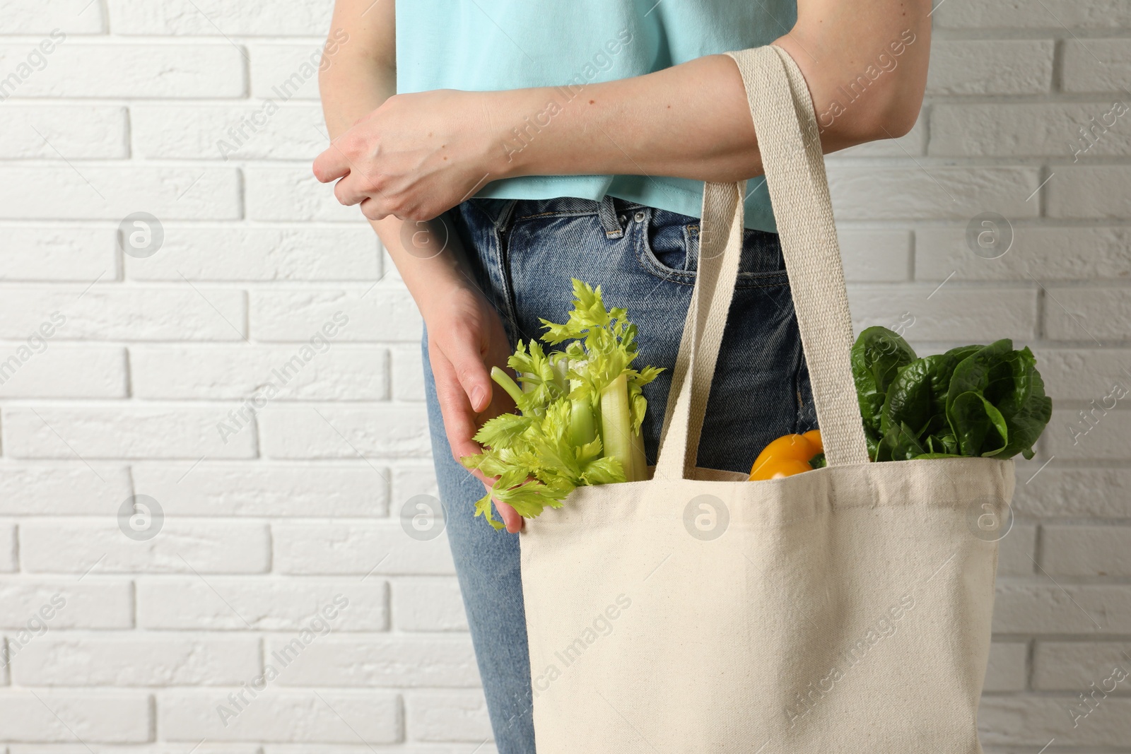 Photo of Woman holding shopper bag with groceries near white brick wall, closeup. Eco friendly lifestyle