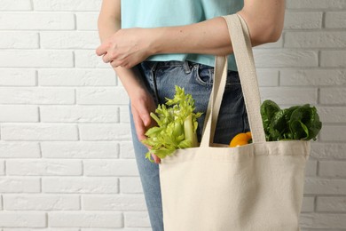 Photo of Woman holding shopper bag with groceries near white brick wall, closeup. Eco friendly lifestyle