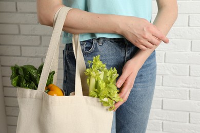 Photo of Woman holding shopper bag with groceries near white brick wall, closeup. Eco friendly lifestyle