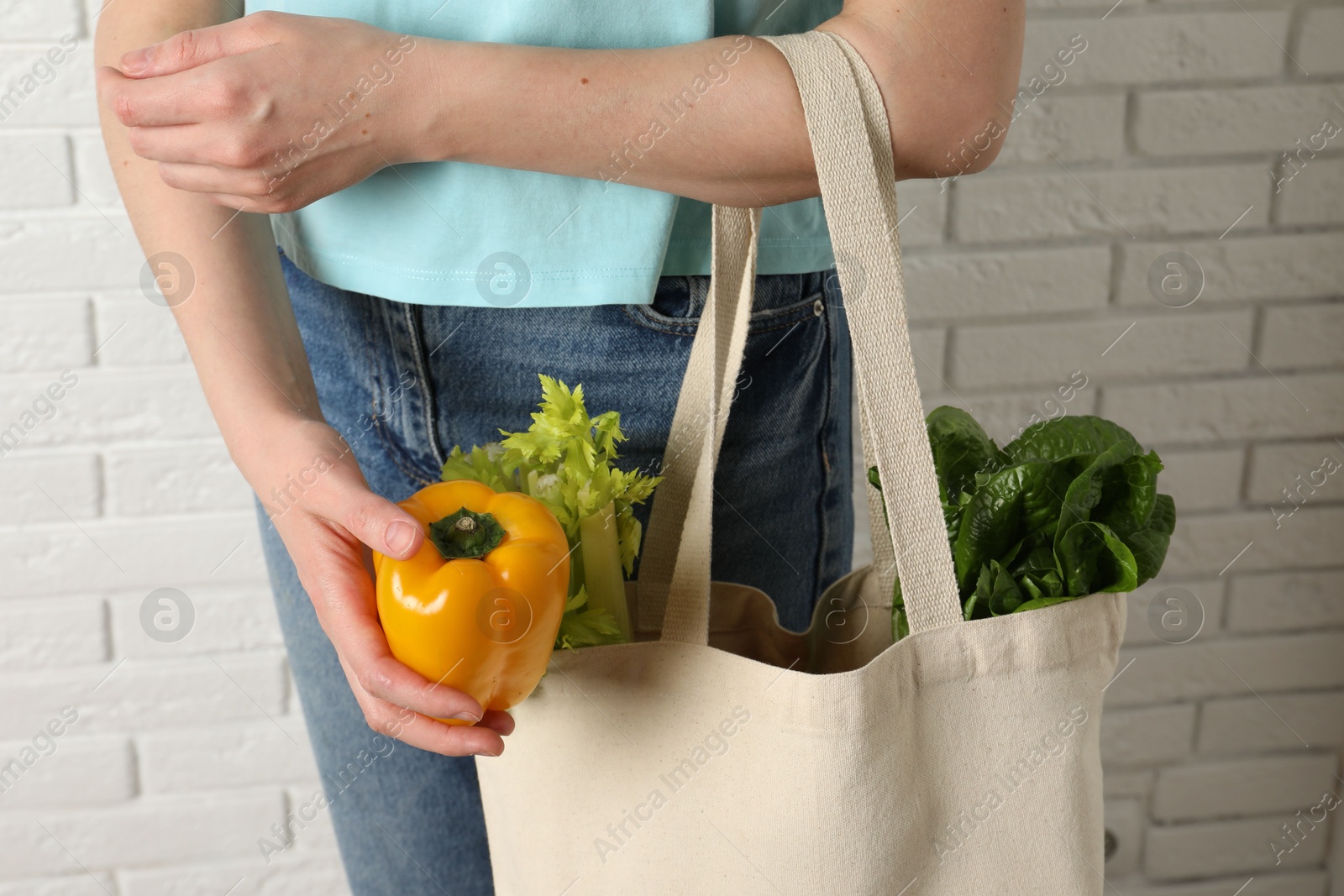 Photo of Woman holding shopper bag with groceries near white brick wall, closeup. Eco friendly lifestyle