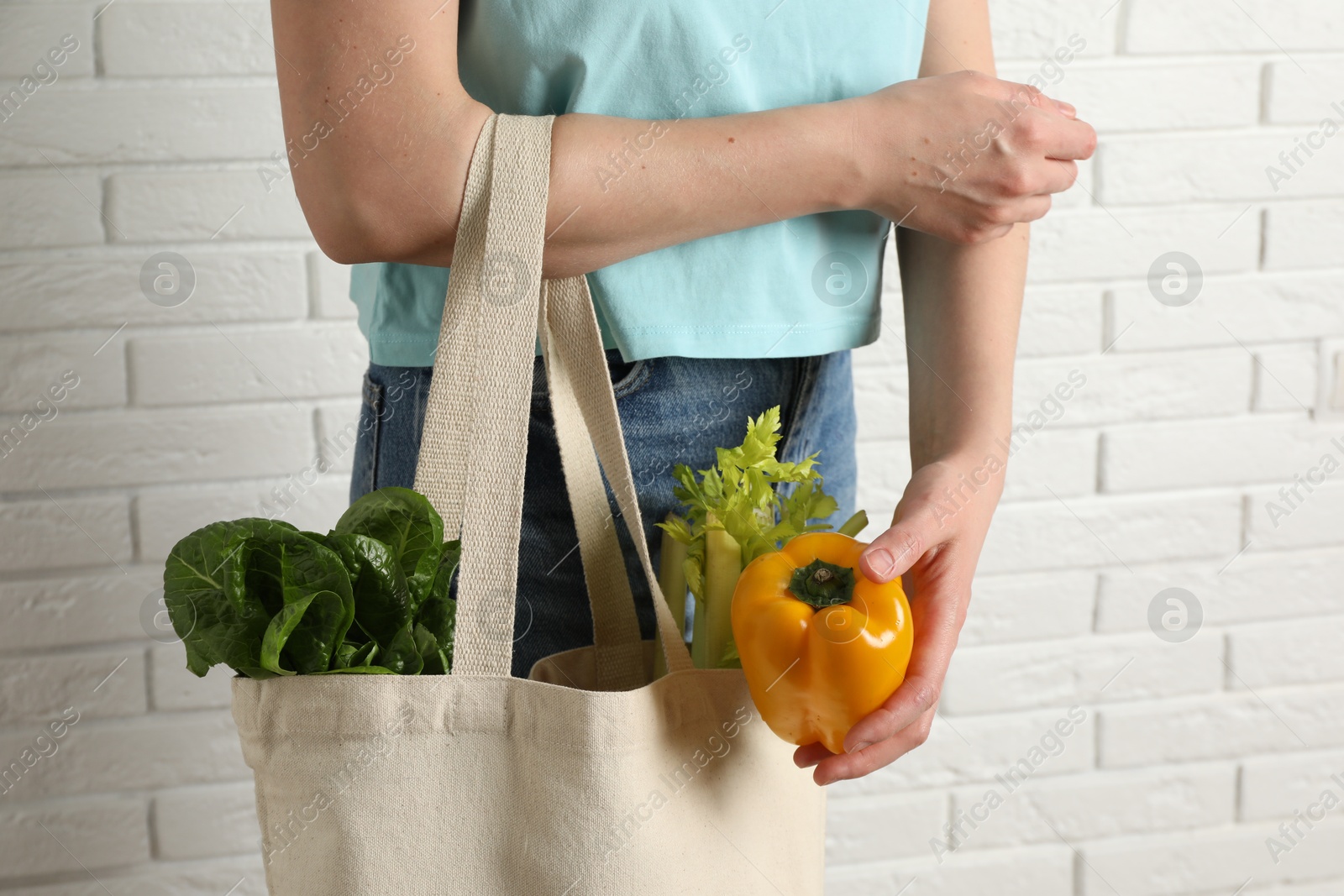 Photo of Woman holding shopper bag with groceries near white brick wall, closeup. Eco friendly lifestyle