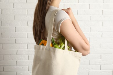 Photo of Woman holding shopper bag with groceries near white brick wall, closeup. Eco friendly lifestyle