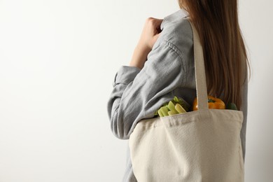 Photo of Woman holding shopper bag with groceries on white background, closeup and space for text. Eco friendly lifestyle