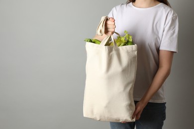 Photo of Woman holding shopper bag with groceries on light grey background, closeup and space for text. Eco friendly lifestyle